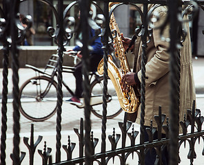 Image showing african street musician playing jazz on saxophone throw lattice 
