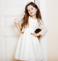 Image showing little cute girl at home, opening door well-dressed in white dre