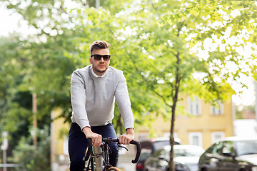 Image showing young man in shades riding bicycle on city street