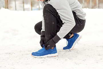 Image showing man with earphones tying sports shoes in winter