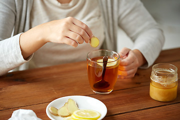 Image showing close up of woman adding ginger to tea with lemon