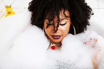 Image showing young afro-american teen girl laying in bath with foam, wearing 