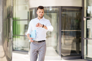 Image showing man with folder looking at wristwatch on street