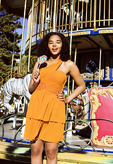 Image showing cool real teenage girl with candy near carousels at amusement pa