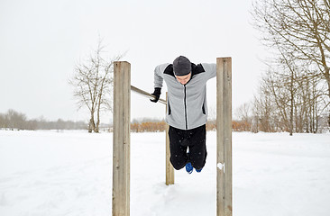 Image showing young man exercising on parallel bars in winter