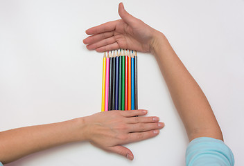 Image showing On a sheet of paper lie pencils Female hands lie above and below them