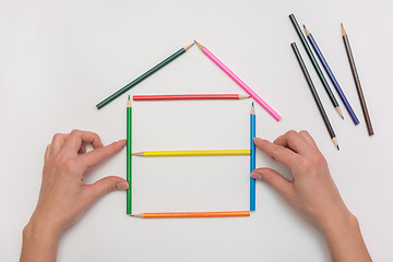 Image showing closeup Hands build a house on a piece of paper from the crayons, erecting walls