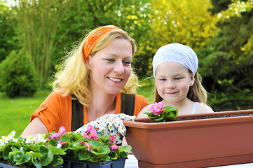 Image showing Young woman and little girl gardening in spring, planting flower seedlings, smiling mother and her happy child working in garden