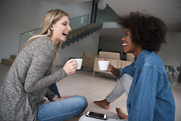 Image showing young multiethnic women sit on the floor and drinking coffee