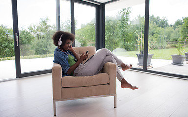 Image showing African american woman at home in chair with tablet and head pho