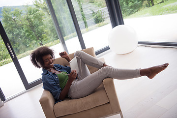 Image showing African american woman at home in chair with tablet and head pho