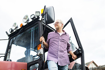 Image showing old man or farmer getting out of tractor at farm