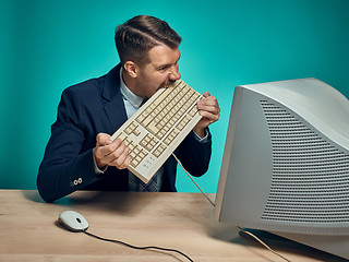 Image showing Angry businessman breaking keyboard against blue background