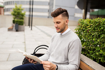 Image showing smiling man reading newspaper on city street bench