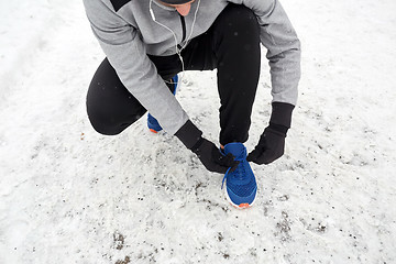 Image showing man with earphones tying sports shoes in winter