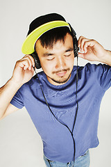 Image showing young asian man in hat and headphones listening music on white b