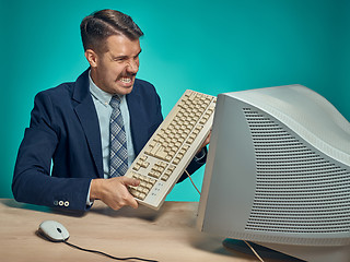 Image showing Angry businessman breaking keyboard against blue background