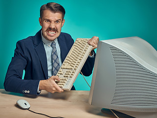 Image showing Angry businessman breaking keyboard against blue background