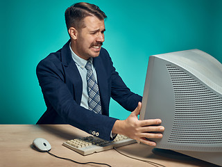 Image showing Angry businessman using a monitor against blue background