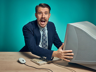 Image showing Angry businessman using a monitor against blue background