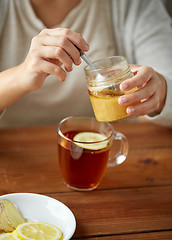 Image showing close up of woman adding honey to tea with lemon