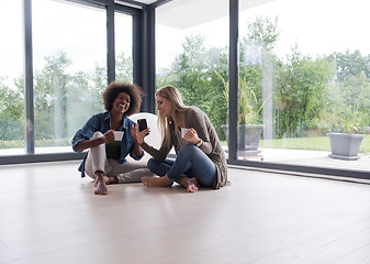 Image showing multiethnic women sit on the floor and drinking coffee