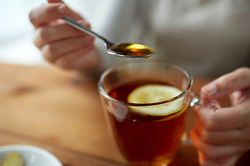 Image showing close up of woman adding honey to tea with lemon