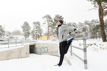 Image showing sports man stretching leg at fence in winter