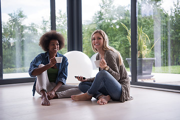 Image showing multiethnic women sit on the floor and drinking coffee