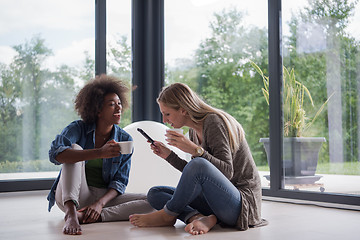 Image showing multiethnic women sit on the floor and drinking coffee