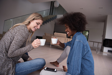 Image showing young multiethnic women sit on the floor and drinking coffee