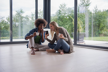 Image showing multiethnic women sit on the floor and drinking coffee