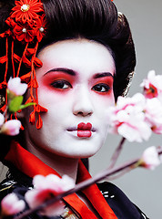 Image showing young pretty geisha in black kimono among sakura, asian ethno