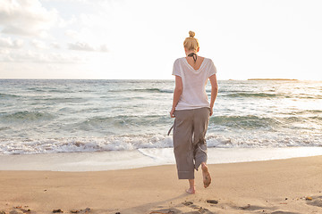 Image showing Woman walking on sand beach at golden hour