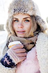 Image showing young pretty teenage hipster girl outdoor in winter snow park having fun drinking coffee, warming up happy smiling, lifestyle people concept