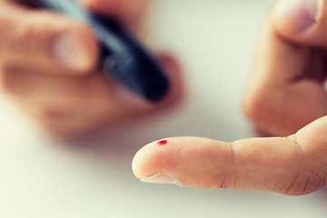 Image showing close up of male finger with blood and glucometer