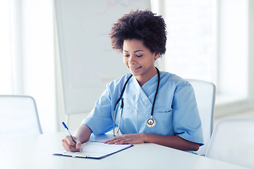 Image showing happy female doctor or nurse writing to clipboard