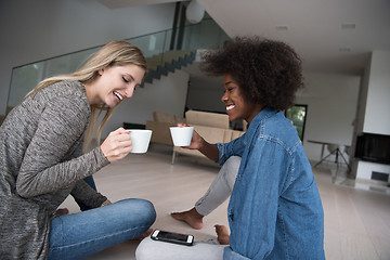 Image showing young multiethnic women sit on the floor and drinking coffee