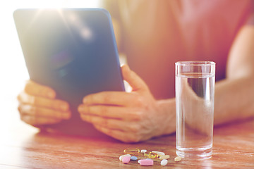 Image showing close up of hands with tablet pc, pills and water