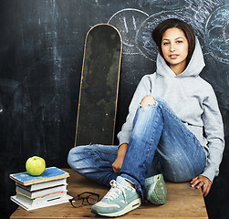 Image showing young cute teenage girl in classroom at blackboard seating on ta