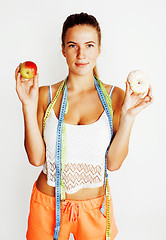 Image showing young blonde woman choosing between donut and apple fruit isolated on white background, lifestyle people concept, measuring tape for diet