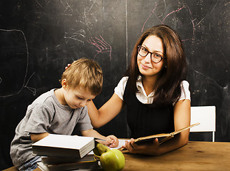 Image showing little cute boy with young teacher in classroom studying at blac