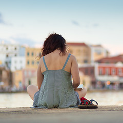 Image showing Rear view of woman sitting on a pier, reading book.