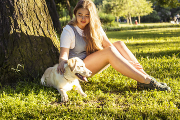 Image showing young attractive blond woman playing with her dog in green park at summer, lifestyle people concept