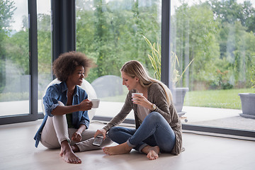 Image showing multiethnic women sit on the floor and drinking coffee