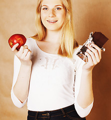 Image showing young beauty blond teenage girl eating chocolate smiling, choice