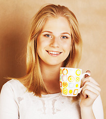 Image showing young cute blond girl drinking coffee close up on warm brown bac