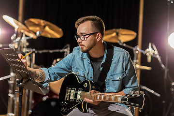 Image showing man with guitar writing to music book at studio