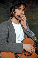 Image showing Cool guy with hat playing guitar on gray background