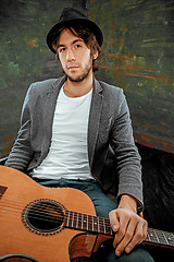 Image showing Cool guy sitting with guitar on gray background